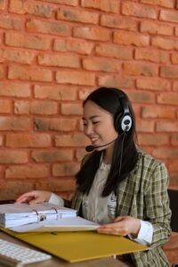 Professional Asian woman wearing a headset, working efficiently at an office with a binder, smiling and focused.